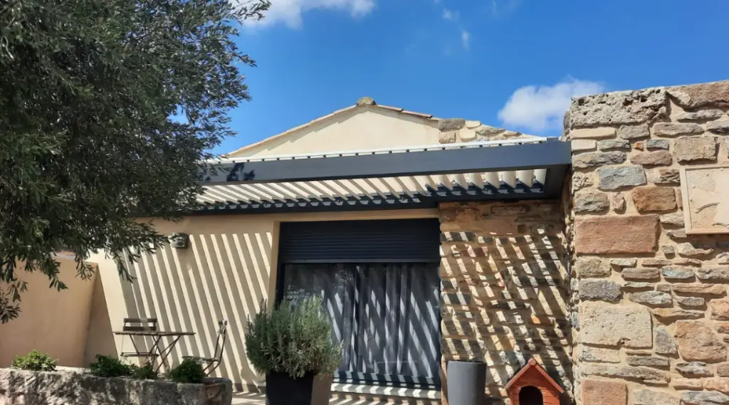 pergola bioclimatique en aluminium sur une maison traditionnelle, elle est adossée à un mur en pierre